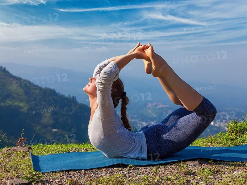 Yoga outdoors, young sporty fit woman doing Ashtanga Vinyasa Yoga asana Dhanurasana, bow pose, in Himalayas mountains in the morning Himachal Pradesh, India