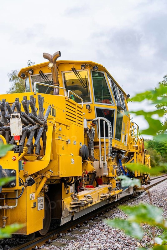 Yellow railway vehicle with technical details and clouds in the sky, tamping machine, Hermann Hessebahn, Calw, Black Forest, Germany