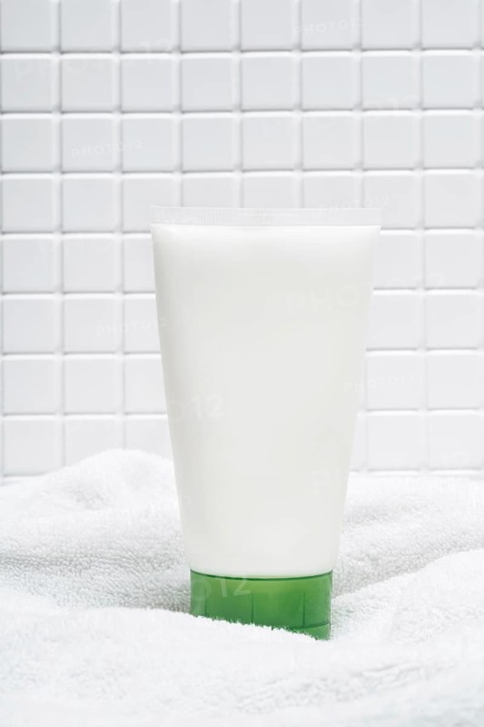 A tube of body care cream on a soft white towel with a tiled bathroom wall in the background, depicting a clean and hygienic skincare environment