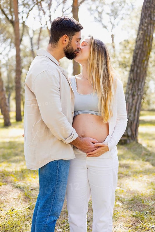 A pregnant woman and her partner share a tender moment outdoors, surrounded by nature's tranquility. They embrace lovingly, capturing the joy and anticipation of new beginnings