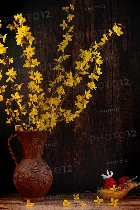 Branches of forsythia in a rustic jug next to Easter decorations against a dark background