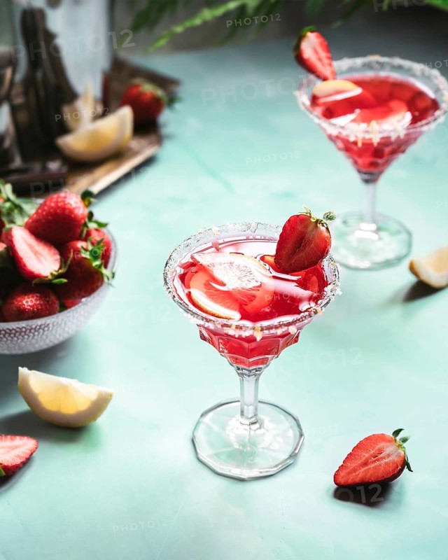 Two elegant glasses of refreshing strawberry cocktail garnished with fresh strawberries and lemon slices on a light teal table, creating a lively and vibrant atmosphere