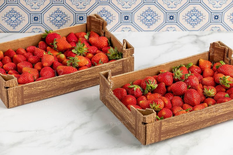 Two boxes of fresh strawberries on a marble slab, blue pattern in the background
