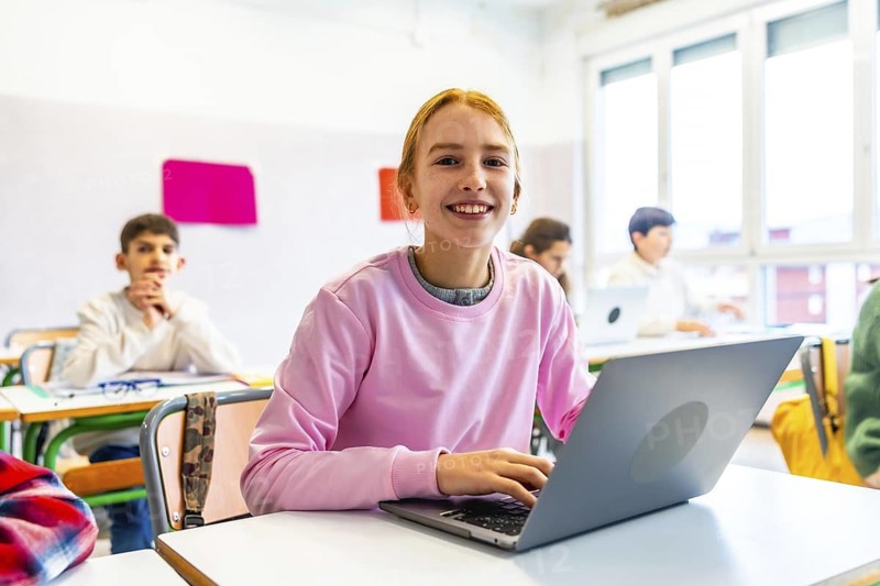 Happy student using a laptop during class, participating in an interactive learning activity with her classmates