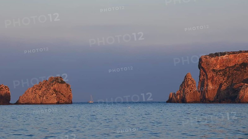 Sunrise over the sea with sailboat and rock formations, morning light, Tsichli Babas islet, Sfaktiria island, Navarino Bay, Pylos, Peloponnese, Greece