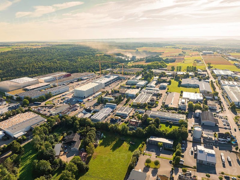 Industrial area with numerous buildings and roads, surrounded by large open fields under a sunny sky, Industrial area Wolfsberg, Nagold, Black Forest, Germany