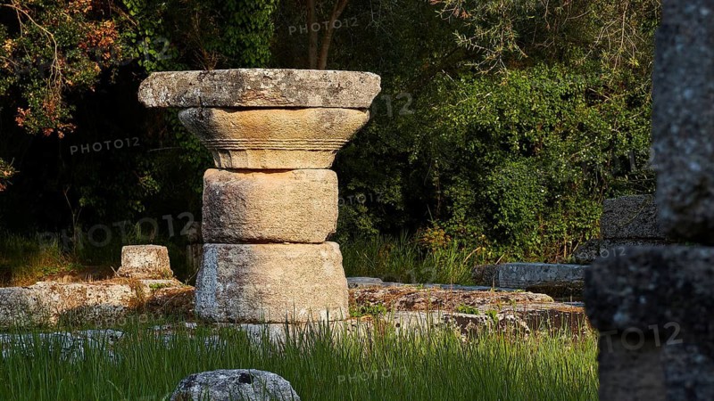 Ancient stone column in shade surrounded by grass and trees, Archaeological Site, Ancient Olympia, Olympia, Peloponnese, Greece