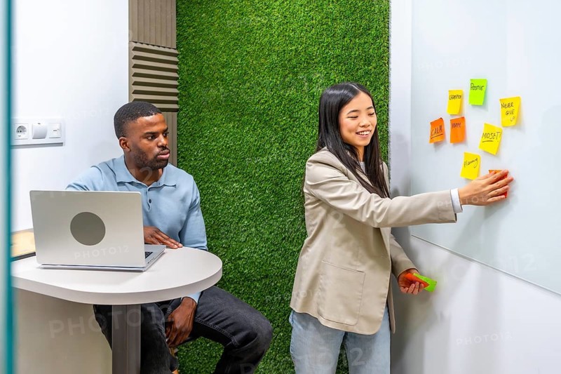 Businesswoman sticking notes on whiteboard during a brainstorming session with her colleague in a modern coworking office