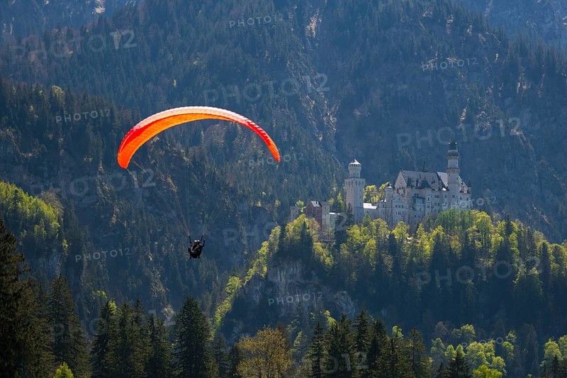 A paraglider flies high above Neuschwanstein Castle in the mountains, Schwangau near Füssen, Ostallgäu district, Swabia, Bavaria, Germany