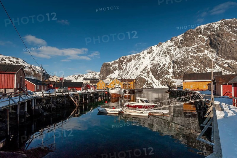 Fishing village with yellow and red houses in front of snow-covered mountains, Nusfjord, Flakstadoya or Flakstadøy, Vestvågøya island, Lofoten, Norway