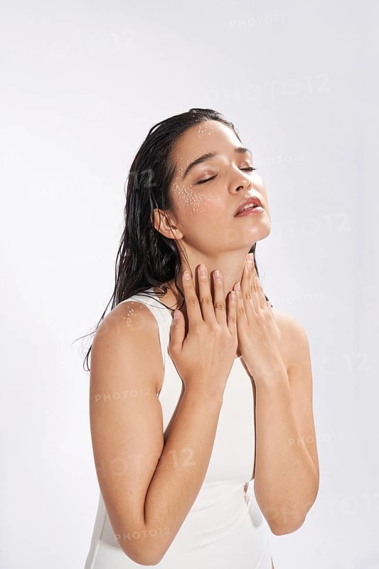 Fresh portrait of a female model in a studio, her eyes closed, with droplets of water on her skin, conveying a serene and refreshing moment