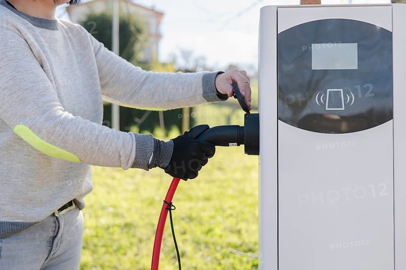 A person is plugging an electric car into a charging station outdoors. The scene highlights sustainable transportation and clean energy solutions for a greener future