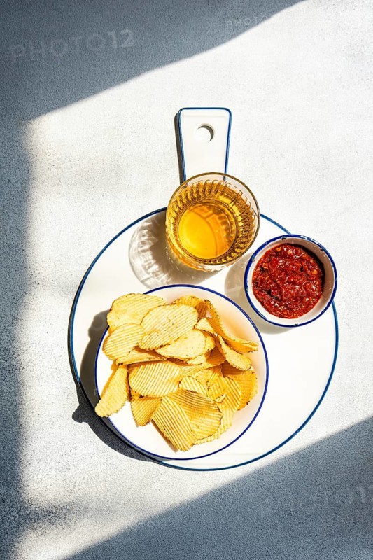 A plate of homemade chips paired with a vibrant salsa dip and a glass of refreshing beverage on a white platter, illuminated by natural sunlight