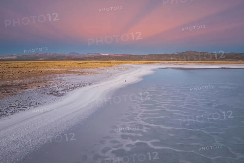 A stunning view of Salinas Grandes, Salta, Argentina, showcasing expansive salt flats under a vibrant pink sunset sky. The serene landscape reflects soft hues and natural beauty