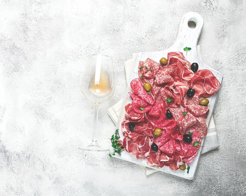 Assorted, meat appetizer, prosciutto, salami and ham, with olives, on a wooden white board, light background, breakfast, top view, close-up, no people
