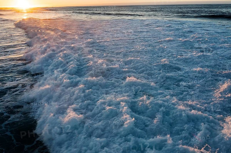 Serene scene with sun gently rising over the crashing waves of Popcorn Beach, Fuerteventura, lighting up the foamy sea