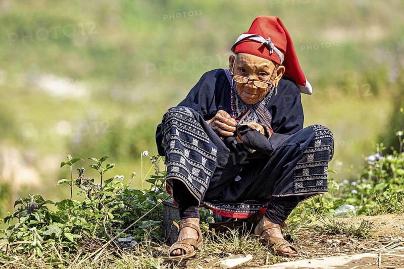 Woman in traditional dress sitting outdoors and doing handicrafts, Large Buddha statue at Fansipan in the mountains near Sa Pa in Vietnam