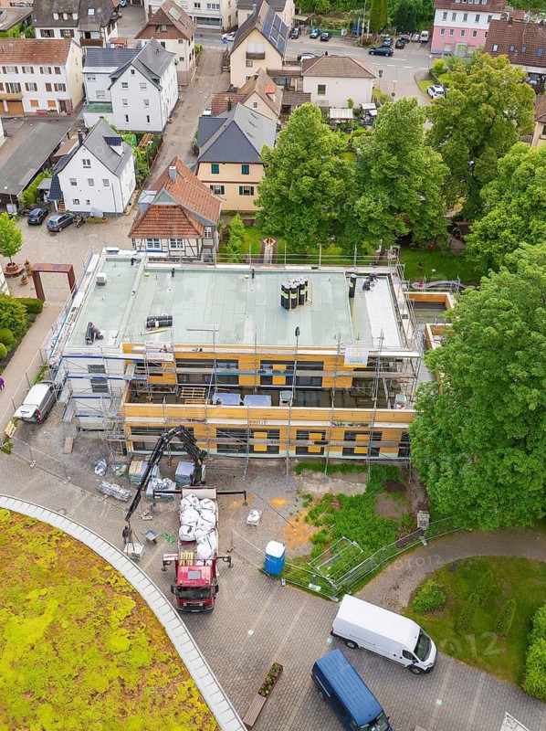 An almost finished building with scaffolding, surrounded by village houses and a parked lorry, new building KITA Calw Hirsau, Black Forest, Germany