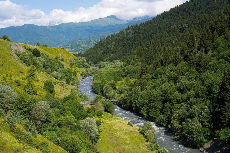 River flows through green mountains and forests with a peaceful summer atmosphere under cloudy skies, Tskheniszqali River near Jakhunderi, Racha-Lechkhumi region and Lower Svaneti, High Caucasus, Georgia