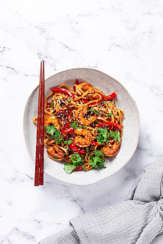 Udon noodles, shrimp with vegetables and fresh herbs, in a bowl with chopsticks, light background, homemade, no people