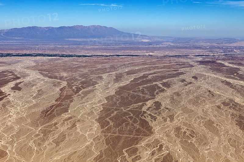 Aerial view of a vast, dry desert with mountains on the horizon under clear blue sky, The landscape and desert near Nasca in the Andes of Peru