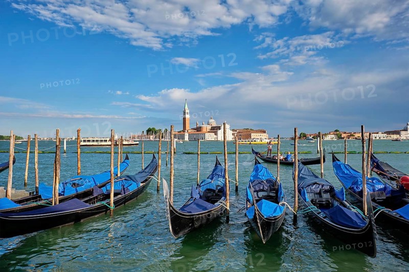 VENICE, ITALY, JUNE 27, 2018: Gondolas and gondolier in lagoon of Venice by Saint Mark (San Marco) square with San Giorgio di Maggiore church in background in Venice, Italy