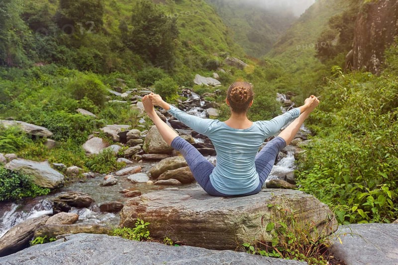 Woman doing Ashtanga Vinyasa asana Upavistha Konasana outdoors at tropical waterfall