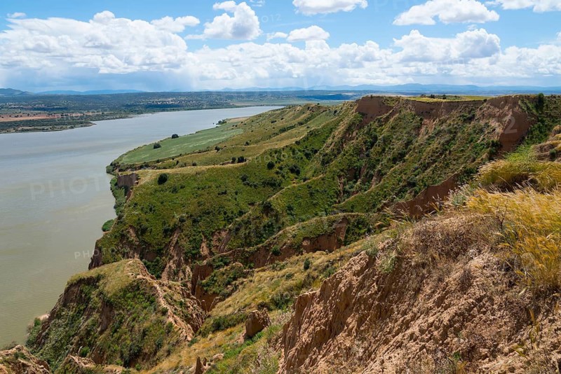 Grüne Hügel und Klippen entlang eines Flusses unter einem blauen Himmel mit weißen Wolken, Barrancas de Burujón, Burujon, río Tajo, Fluss Tajo, embalse de Castrejón, Stausee de Castrejon, Toledo, Kastilien-La Mancha, Spanien