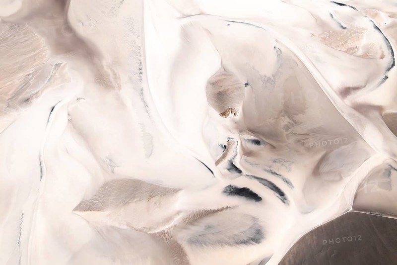 Captivating aerial view showcases swirling, abstract desert patterns whit dunes. Soft shades of beige and tan create an ethereal landscape, resembling a natural artwork