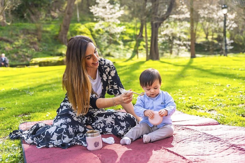 Young mother feeds her baby during a picnic in a park on a beautiful sunny day, enjoying quality time together outdoors