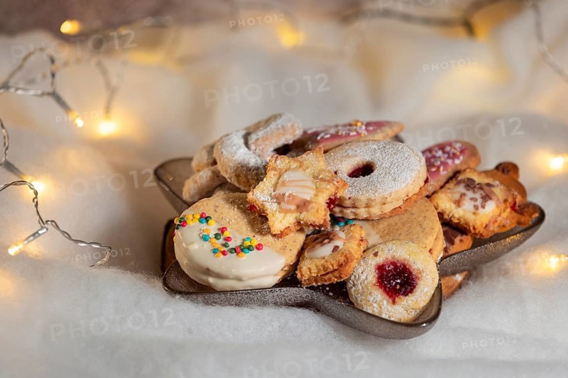 A plate with various Christmas biscuits on white, fairy lights in the background