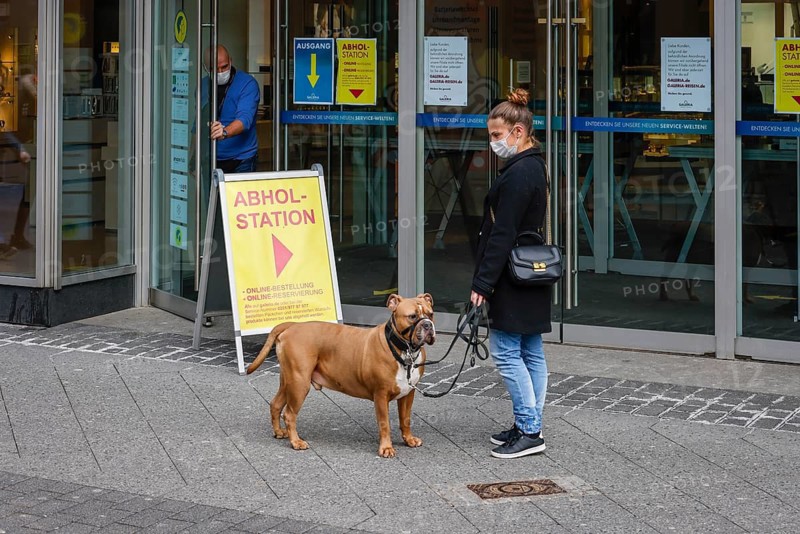 Krefeld, North Rhine-Westphalia, Germany - Krefeld city centre in times of the corona crisis during the second lockdown, most shops are closed, a woman with a dog is waiting at the Galeria Kaufhof Karstadt pick-up station, only a few passers-by are walking on Hochstraße, the main shopping street