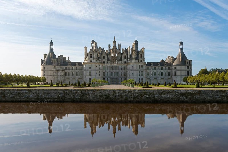 Impressive castle building with towers and windows, reflected in the calm water of the canal, under a blue sky, Chambord Castle, Château de Chambord, Loire Castle, Loire Valley, Department Loir-et-Cher, Region Centre, France