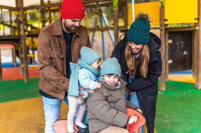 Smiling family enjoying a winter day at the playground, playing together on a rocking horse