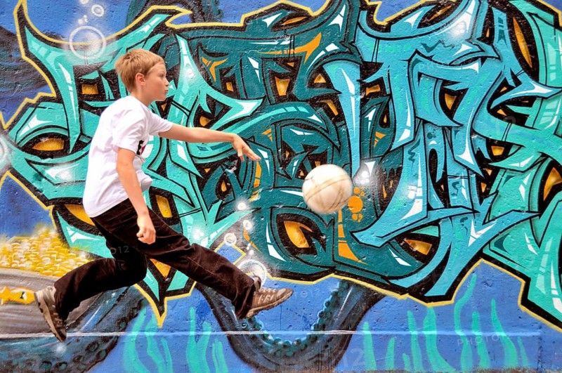 A ten-year-old boy plays with his football in front of a graffiti wall, football pitch in Germany