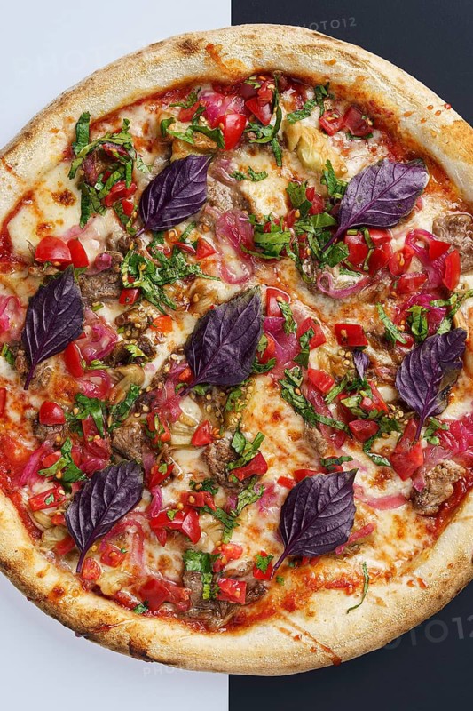 Top view of a freshly baked pizza topped with tomato sauce, mozzarella, lamb, baked eggplant, tomato salsa, sweet onion, tomato sauce and garnished with purple basil leaves