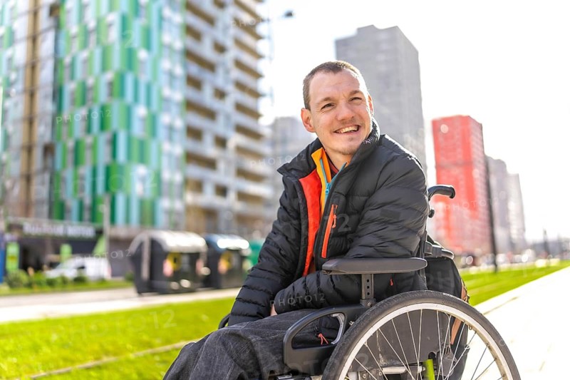 Portrait of a cheerful young disabled man in a wheelchair enjoying a sunny day in the city