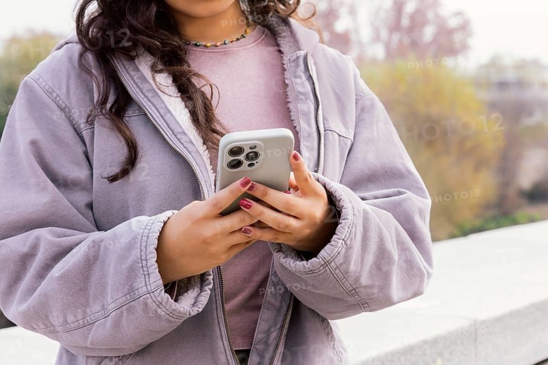Woman enjoying a casual day outdoors, holding a smartphone, dressed in a cozy jacket The scene captures a moment of relaxation and digital connection