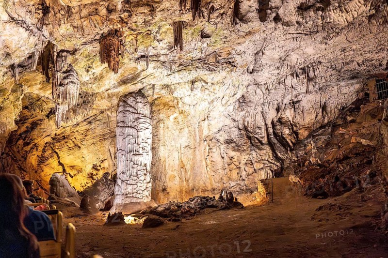 Tourists riding a train inside postojna cave, admiring the stalactites and stalagmites formations