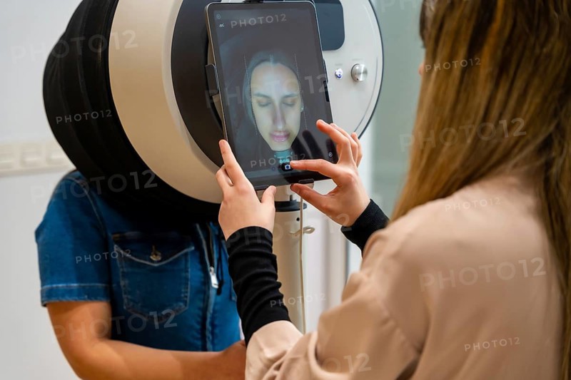 Aesthetic center technician using a modern skin analysis device with a tablet display, performing a facial mapping on a woman to provide personalized skincare and beauty treatment recommendations