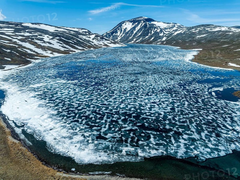 Melting ice on mountain lake Bessvatn, Mt. Besshö, old snow in early spring, aerial view, Jotunheimen National Park, Norway