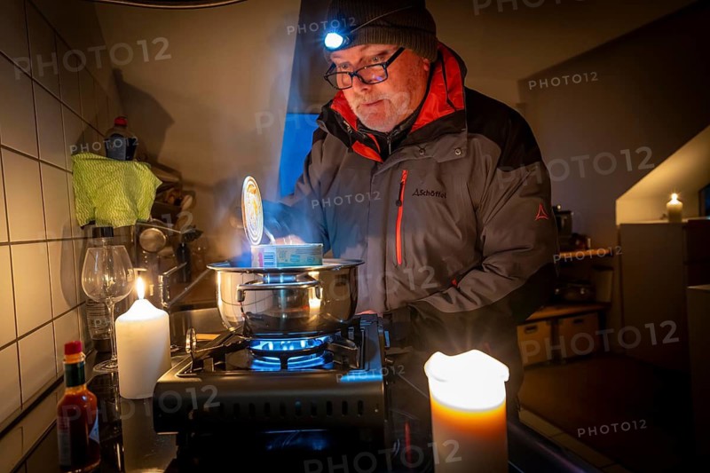 Symbolic picture blackout, extensive, prolonged power failure, in private settings, without electricity, heating, water, cooking in the kitchen, heating food with a gas-powered camping stove, which is also approved for indoor use
