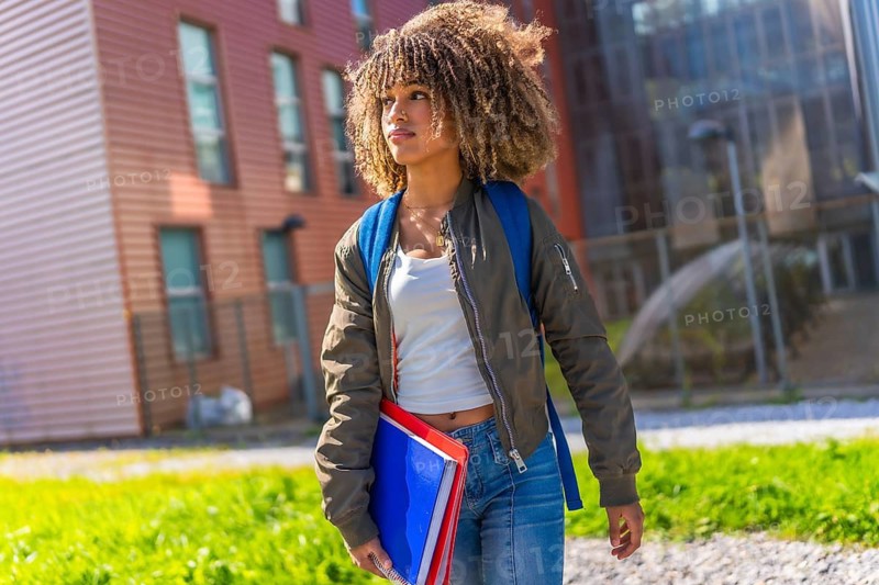 Urban female latin student with curly hair standing distracted outside the university
