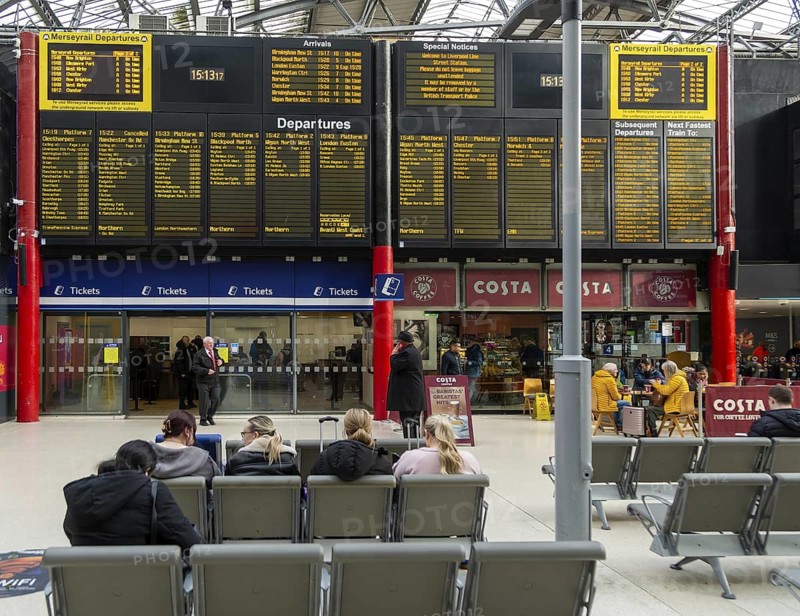 People sitting in seats by electronic information board in concourse area of Lime Street railway station, Liverpool, England, UK