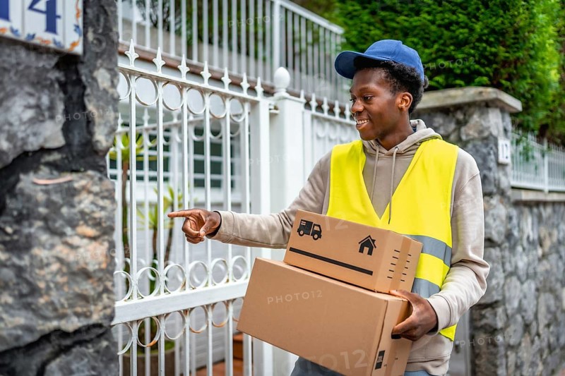 Delivery african young man ringing the doorbell of a house with packages to deliver