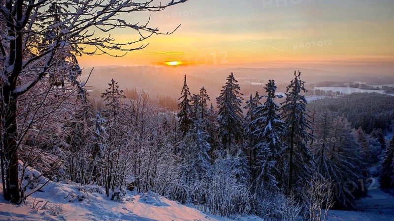 View from Döbra Berg, wide winter landscape with spectacular orange sunset with snow and trees, Franconian Forest nature park Park