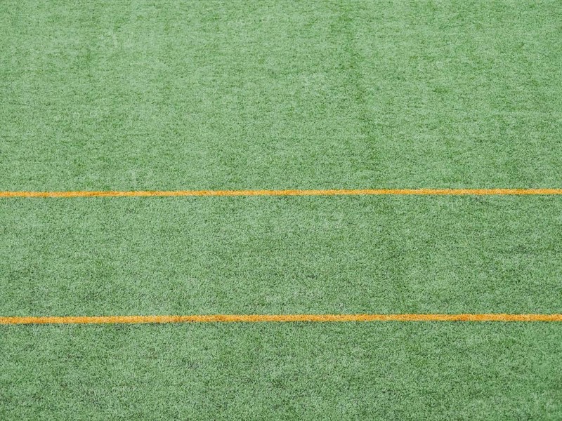 Close up view of green artificial turf featuring parallel yellow lines. Ideal for soccer fields, emphasizes texture and vibrant color. Suitable for design and backgrounds