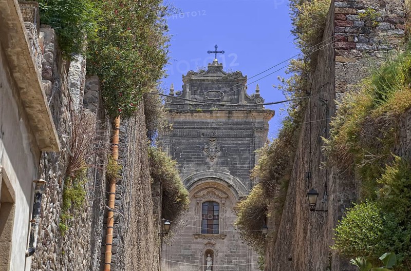 Narrow alley in an old town leading to San Bartolomeo Cathedral with a cross on the roof, Lipari city Aeolian Islands Sicily Italy