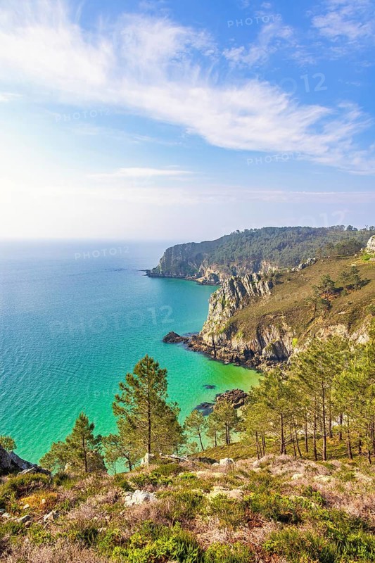 Scenic coastal landscape with steep rocky cliffs covered in green vegetation overlooking a turquoise sea a sunny summer day, Crozon peninsula, Bretagne, France