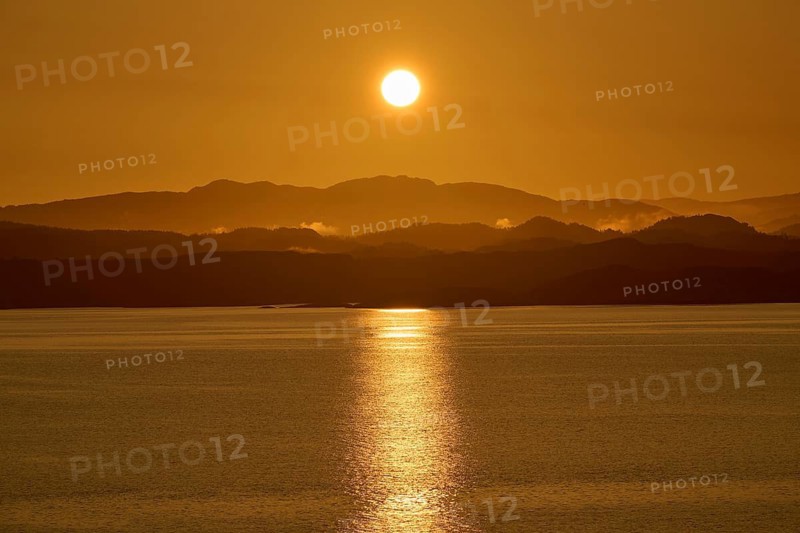 A soft orange sunrise behind the dark silhouettes of mountains and a calm sea, sunbeams reflecting in the sea, autumn, Bergen, North Sea, Norway